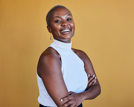 Portrait of a laughing young African businesswoman with short hair standing in front of a yellow background