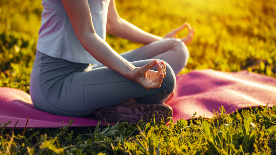 Woman doing yoga outdoors at sunrise in lotus position.