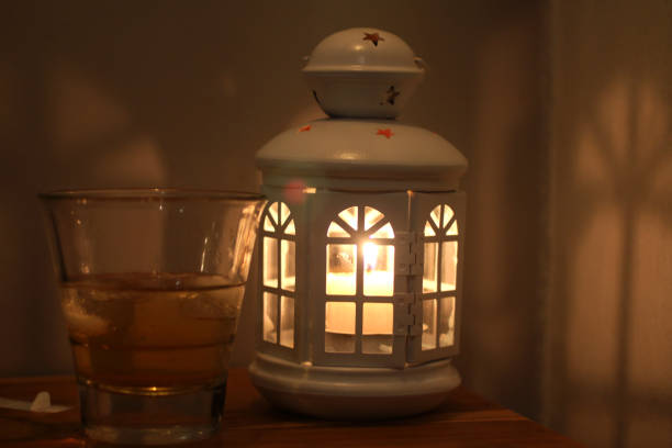 White lantern and the candle light inside with its shadow in the room at night. Classic lantern with handle. Be the light concept. Hope and faith concepts.