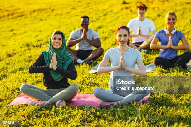 Diverse multiracial people meditating in lotus pose and doing gesture on their outdoor yoga class.
