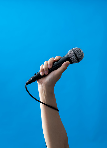 Hand holding a microphone on blue background.
