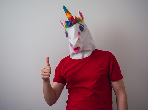 Man in rainbow colored unicorn mask with thumbs up and copy space