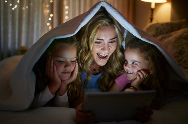 istock Young happy caucasian mother using a digital tablet with her little daughters before bedtime at home. Cute comfy siblings watching a movie on a digital tablet with their mom 1398120640