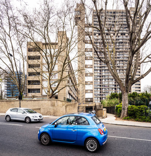 Driving past the Trellick Tower London, UK - Small hatchback cars passing on a street in front of the Trellick Tower in Kensal Green, London. trellick tower stock pictures, royalty-free photos & images