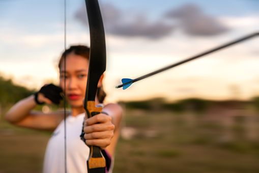 young female archer, archery, shoot arow with bow in nature field to target, success concept, at field for sport exercise at sunset time