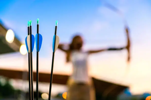 young female archer, archery, shoot arow with bow in nature field to target, success concept, at field for sport exercise at sunset time