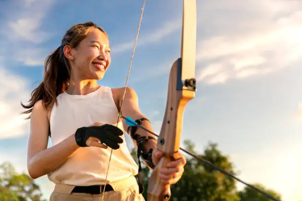 Photo of young female archer, archery, shoot arow with bow in nature field to target, success concept, at field for sport exercise at sunset time