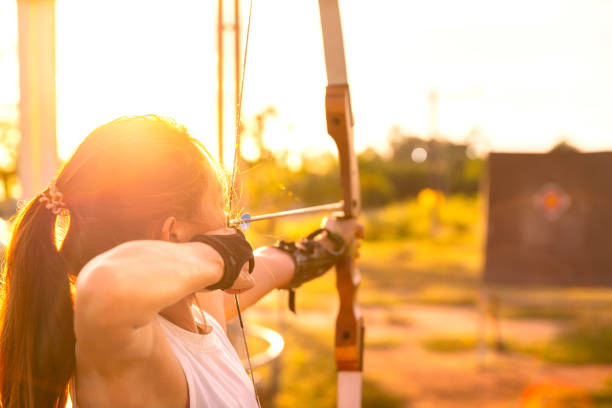 arqueiro jovem, arco e flecha, tiro arow com arco no campo da natureza para o alvo, conceito de sucesso, em campo para exercício esportivo no tempo do pôr do sol - archery bow arrow women - fotografias e filmes do acervo