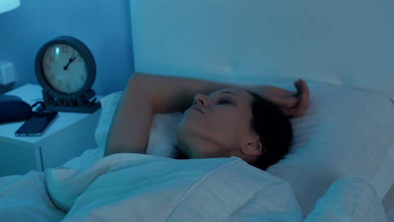 Woman lying in bed and check time in clock suffering from insomnia