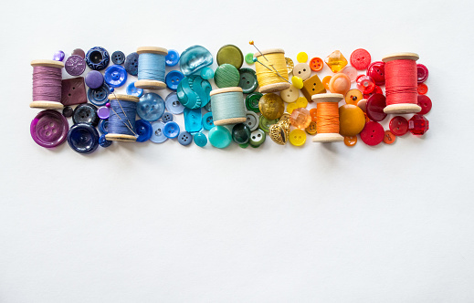 A lot of buttons and reels with colorful threads, laid out on a white background in the colors of the rainbow. Copy space.