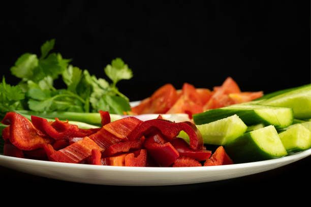 primer plano de hierbas y verduras frescas picadas en un plato blanco sobre un fondo negro. pepinos, tomates, pimientos, cebollas verdes, gallo. vitaminas útiles de las verduras - chopped green bell pepper pepper bell pepper fotografías e imágenes de stock