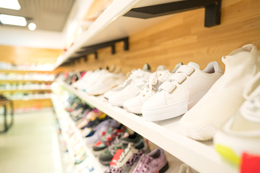 Shelves with different white and multicolored footwear at shoes store - new fashion collection at fashionable shop. Reselling concept. Shoes stall against blurred store background with copy space