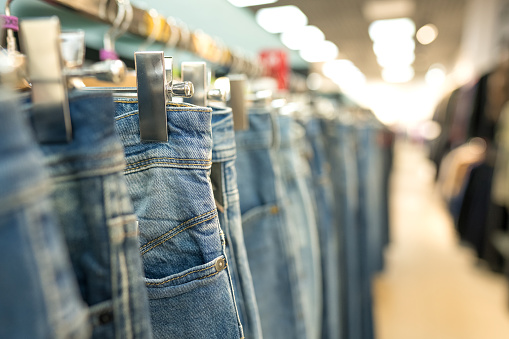 Jeans on hangers - new fashion collection at fashionable clothes store. Clothing rental or reselling concept. Clothes stall against blurred store background with copy space