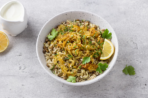 Traditional Middle Eastern dish, Mujadara of lentils, rice and fried onions with lemon and herbs on a light gray background, top view