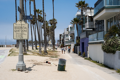 Los Angeles, USA - May 17th, 2022: A person sleeping on Venice Beach early in the morning by a residential quiet zone sign.