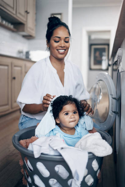 Shot of a young mother playfully bonding with her baby girl while doing the laundry at home Here to help mom laundromat laundry residential structure cleaning stock pictures, royalty-free photos & images