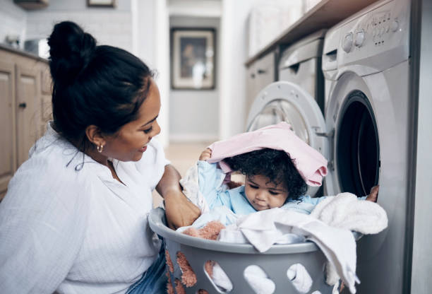 Shot of a young mother playfully bonding with her baby girl while doing the laundry at home Where are you hiding? laundromat laundry residential structure cleaning stock pictures, royalty-free photos & images