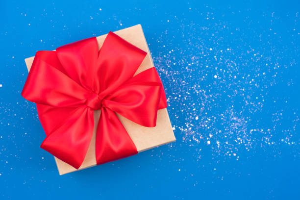 istock Christmas present box with red ribbon bow on blue backgrounds with sparkles around. Beautiful Christmas and New Year festive background with copy space. Gift box 1398131309