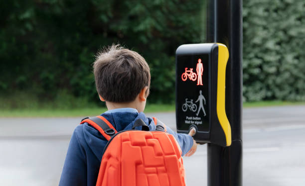 portrait en vue arrière écolier appuyant sur un bouton aux feux de circulation sur le passage pour piétons sur le chemin de l’école. garçon enfant avec sac à dos utilisant des installations piétonnes contrôlées par les feux de circulation pour t - sign street traffic left handed photos et images de collection