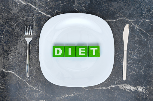 The concept of a diet. Empty white plate with a fork and a table knife on a dark marble background