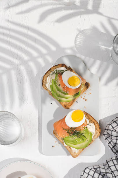 istock Summer healthy lunch, breakfast with light soft cheese sandwich, red fish, avocado and egg. Tropical shadows, sunlight, white background. Aesthetic still life, healthy food concept 1398132893
