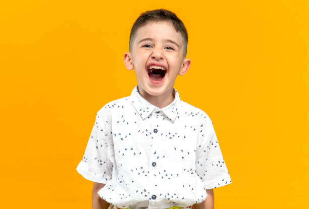 portrait of a cute little boy posing and laughing against a yellow background stock photo