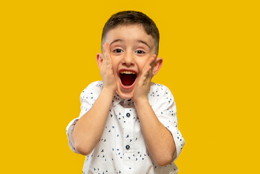 portrait of a cute little boy posing and laughing against a yellow background
