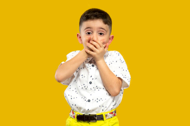in front of the yellow background,the shocked and surprised child looking at the camera stock photo