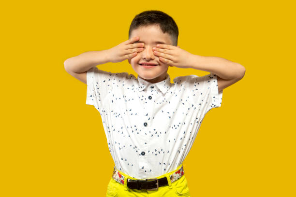 in front of the yellow background,the boy, who closes his eyes with his hands , not wanting to see, stock photo