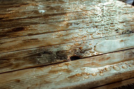 background of lacquered burnt wood texture with shiny water drops and and puddles from the rain, wet wooden planks