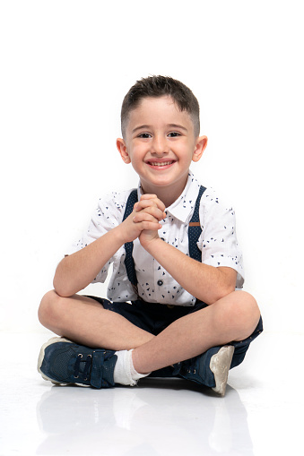 Cute little boy is sitting on the floor against the white background , confident , determined , smiling