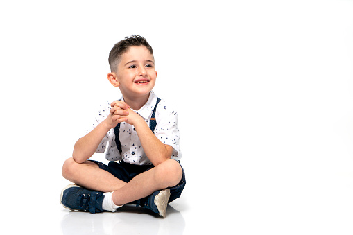 Cute little boy is sitting on the floor against the white background , confident , determined , smiling