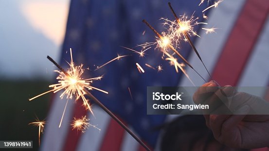 istock Happy 4th of July Independence Day, Hand holding Sparkler fireworks USA celebration with American flag background. Concept of Fourth of July, Independence Day, Fireworks, Sparkler, Memorial, Veterans 1398141941