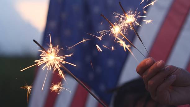 happy 4th of july independence day, hand holding sparkler fireworks usa celebration with american flag background. concept of fourth of july, independence day, fireworks, sparkler, memorial, veterans - dia da independência imagens e fotografias de stock