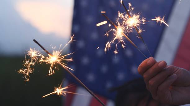 Happy 4th of July Independence Day, Hand holding Sparkler fireworks USA celebration with American flag background. Concept of Fourth of July, Independence Day, Fireworks, Sparkler, Memorial, Veterans feliz 4 de julio día de la independencia, sosteniendo de la mano sparkler fuegos artificiales de celebración de ee.uu. con fondo de bandera estadounidense. concepto de cuatro de julio, día de la independencia, fuegos artificiales, bengala, memorial, vet