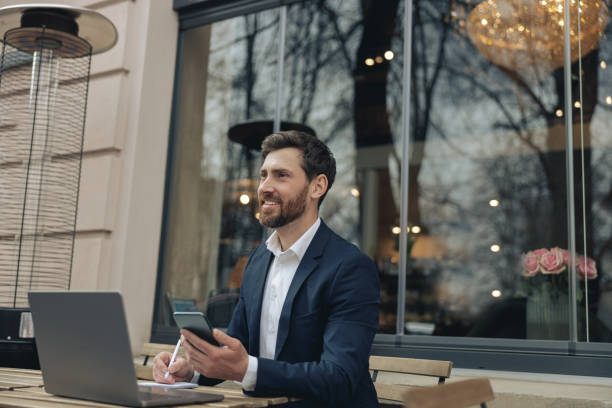 istock Happy businessman with laptop in cafe, mobile phone and notebook. Taking notes and planning. 1398144589