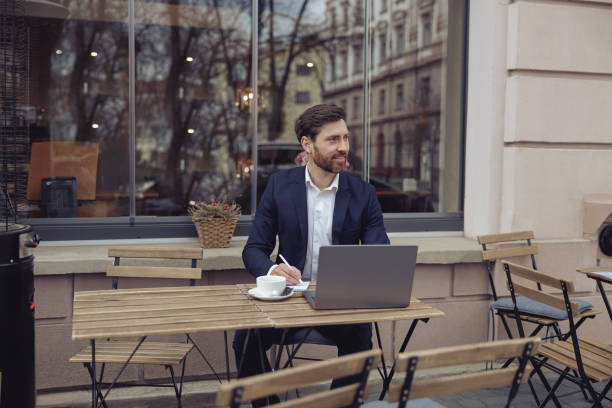istock Handsome businessman taking notes while working at laptop in cafe outdoors. Coffee break. 1398144601