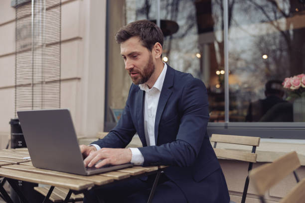 istock Caucasian handsome businessman working at laptop outdoors in cafe. Texting on keyboard. 1398144603