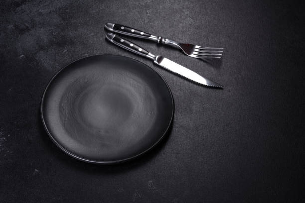 istock Black plate on a black background. Flat lay, top view, copy space 1398146511