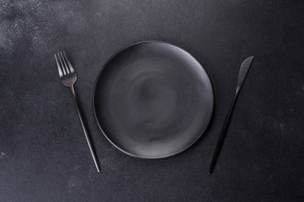 istock Black plate on a black background. Flat lay, top view, copy space 1398146563