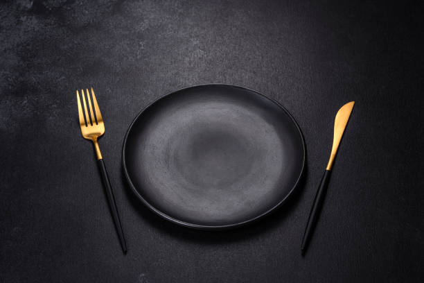 istock Black plate on a black background. Flat lay, top view, copy space 1398146564