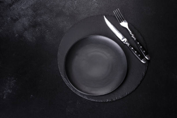 istock Black plate on a black background. Flat lay, top view, copy space 1398146655