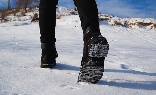 A teenage girl in black jeans and boots walks uphill through the dense snow. Close-up shot of the legs from behind.