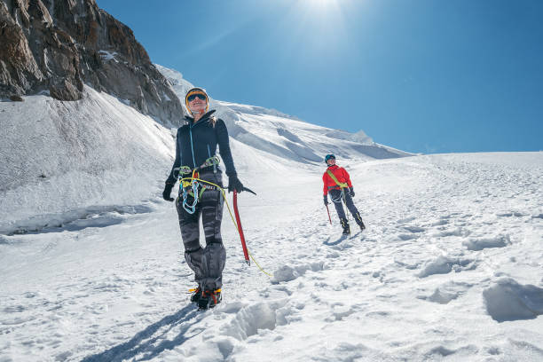 モンブラン・デュ・タクル・サミット4248mを降りる2人の笑う若い女性ロープチームは、雪の斜面を歩く氷の斧で登山服を着ていました。人々の極端な活動スポーティなコンセプトイメージ。 - アイスクライミング ストックフォトと画像