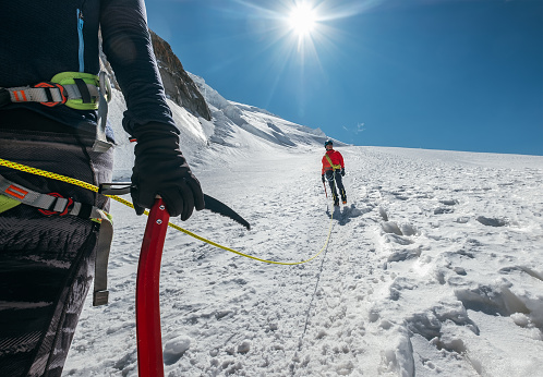 Rope team descending Mont Blanc (Monte Bianco) summit 4,808m dressed mountaineering clothes walking by snowy slopes with ice axe Climbing harness and green dynamic rope on the close up foreground.