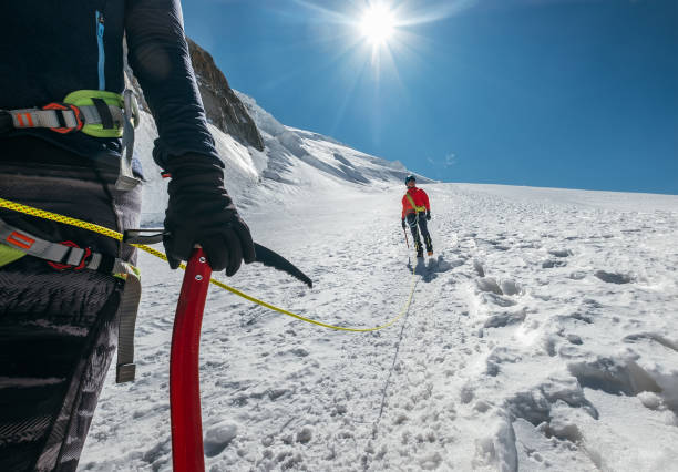 equipe de corda descendo mont blanc (monte bianco) cume 4.808m vestido de roupas de montanhismo andando por encostas nevadas com machado de gelo escalar arreios e corda dinâmica verde em primeiro plano. - ice axe - fotografias e filmes do acervo