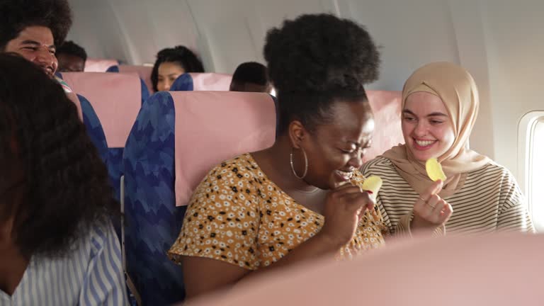 Friends sitting next to each other on an airplane chatting back and forth and sharing snacks