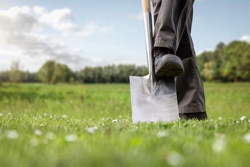 Low angle view of a green meadow with a spade and the feet of a person. Concept for groundbreaking ceremony or gardening in general.