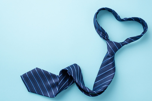 Father's Day concept. Top view photo of heart shaped blue necktie on isolated pastel blue background with copyspace
