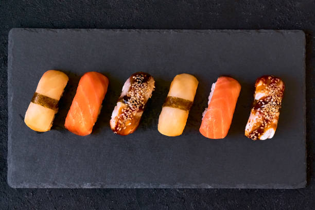 Assorted sushi with salmon, eel and escolar on black stone plate on dark background. Minimal concept.